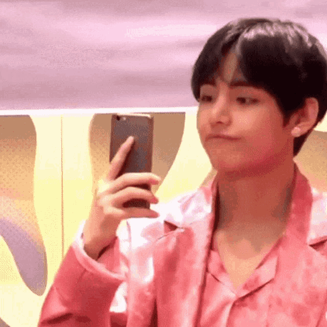 a young man in a pink shirt is taking a picture of himself with his phone .