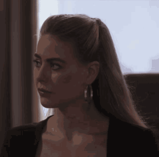 a woman wearing hoop earrings and a black top looks to the side