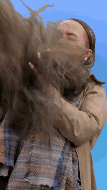 a woman in a trench coat is blowing dust from her hair