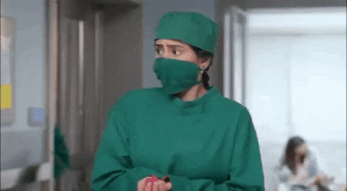 a female surgeon wearing a surgical gown and mask is standing in a hospital hallway .
