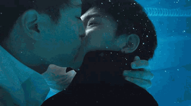 two men are kissing underwater in a pool with a blue background
