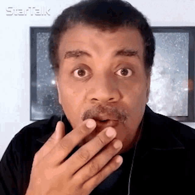 a man with a surprised look on his face is wearing headphones and covering his mouth with his hand .
