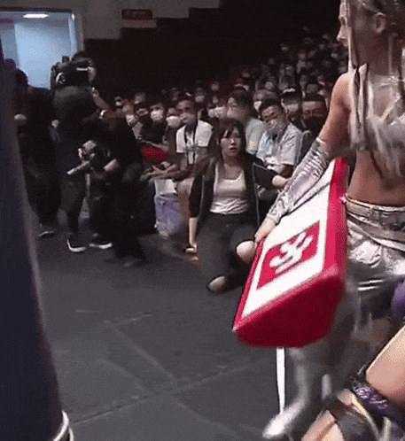 a woman is kneeling down in front of a crowd while holding a red and white sign that says ' s '