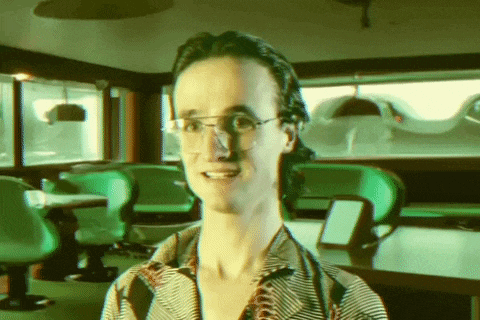 a man wearing glasses and a striped shirt smiles in a green room