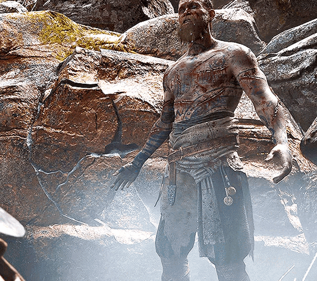 a man with a beard is covered in mud and standing in front of rocks