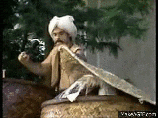 a man in a turban is sitting on top of a barrel holding a snake .