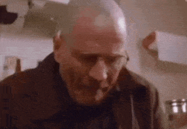 a bald man wearing glasses is standing in a kitchen .