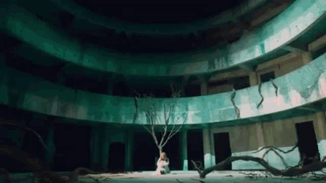 a woman is sitting in a dark room with a tree in the middle .