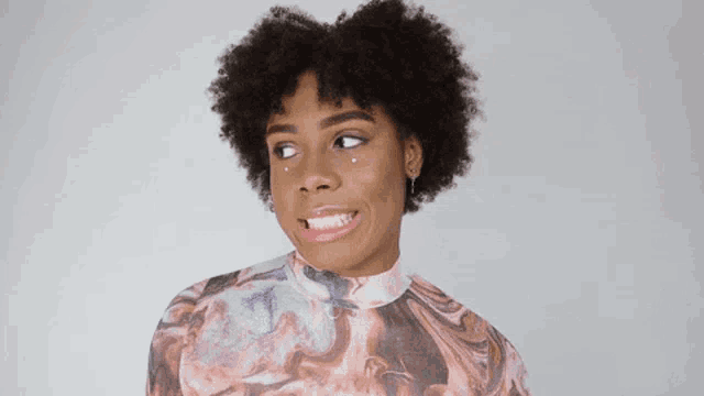a woman with curly hair is making a funny face while wearing a colorful shirt .