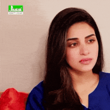a woman in a blue shirt is sitting in front of a jhalka beauty cream ad