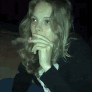 a woman with long hair is smoking a cigarette in a dark room