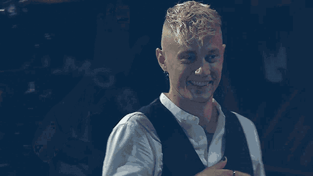 a man with blonde hair wearing a white shirt and a black vest