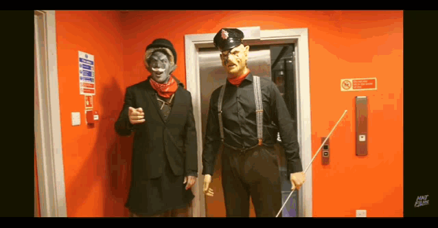 two men standing in front of an elevator with a no smoking sign on the door