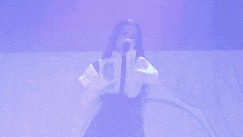 a woman singing into a microphone with a purple background