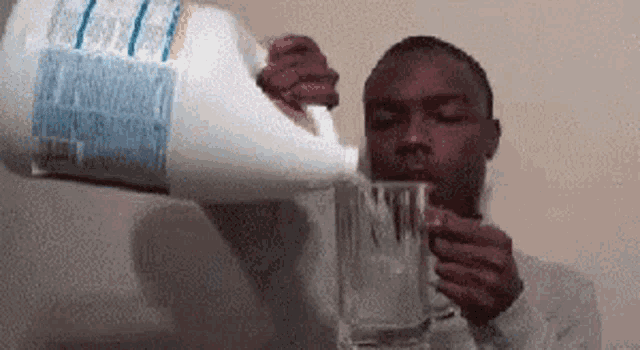 a man is pouring milk into a glass while holding a gallon of milk .