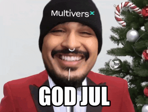 a man wearing a beanie that says multivers on it is smiling in front of a christmas tree