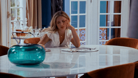 a woman sits at a table with a blue vase on it