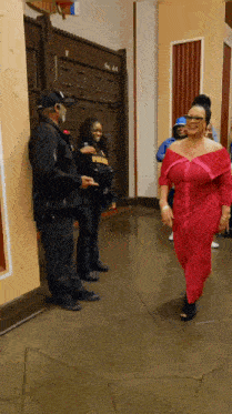 a woman in a red dress is walking down a hallway next to a man in a black jacket with the word police on it