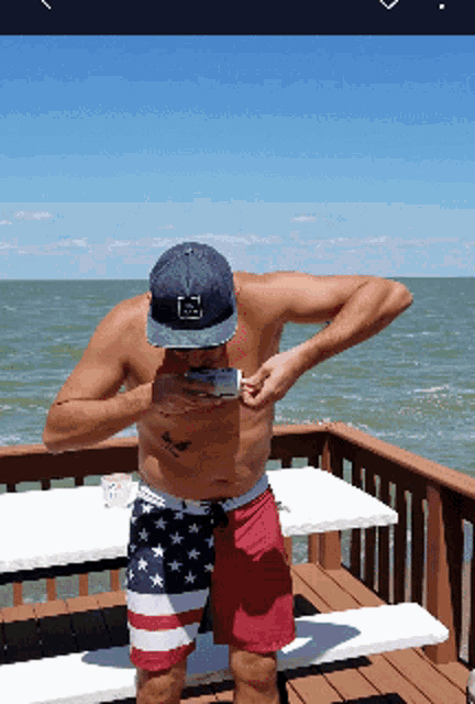 a shirtless man standing on a deck looking at his cell phone