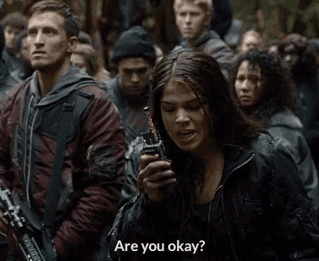 a woman holding a walkie talkie says " are you okay " in front of a crowd of people