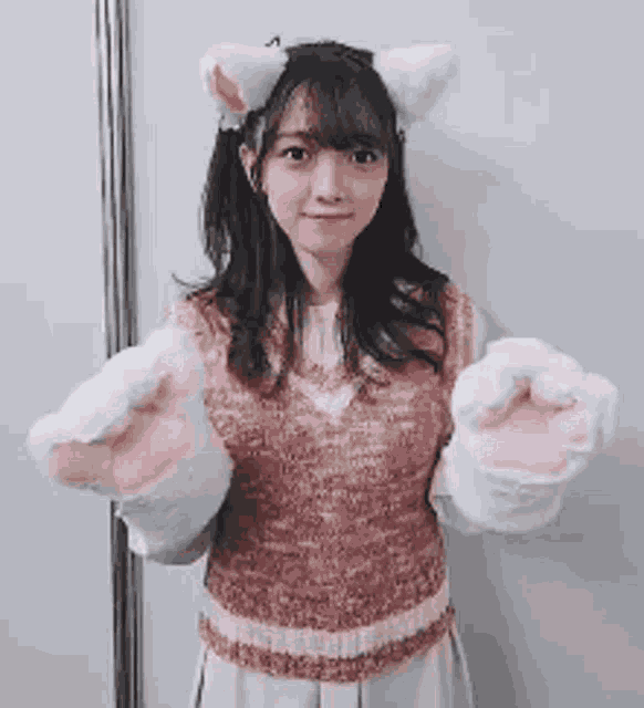 a girl wearing cat ears and paws is holding her hands up in the air .