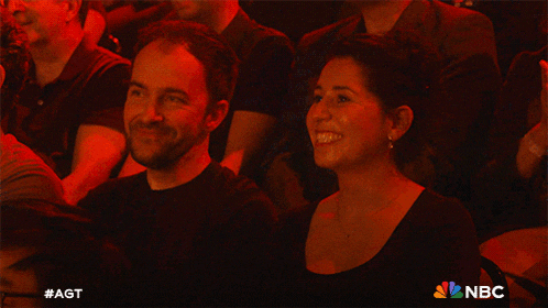 a group of people sitting in a dark room with a nbc logo on the bottom