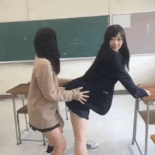two girls are standing next to each other in a classroom and one is touching the other 's butt .