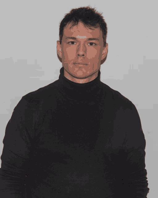 a young man wearing a black turtleneck sweater looks at the camera