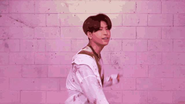 a man is standing in front of a pink brick wall wearing a tie dye shirt and a white jacket .