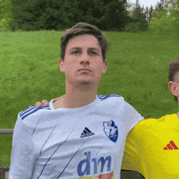 a man in a white adidas shirt stands next to another man in a yellow adidas shirt