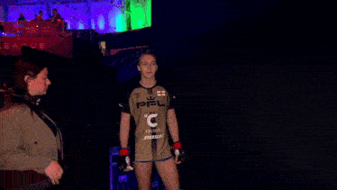 a woman wearing a celsius bose shirt walks through a dark hallway