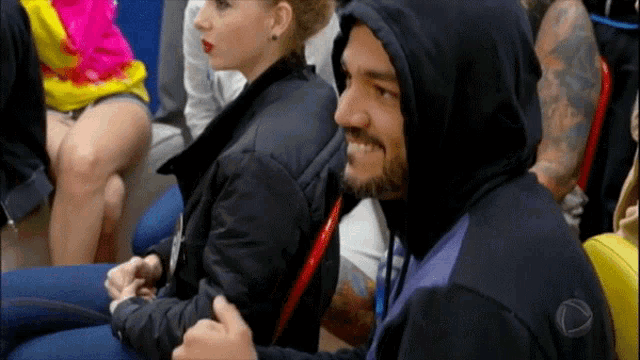 a man in a hooded jacket sits in a crowd of people