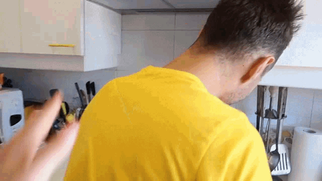 a man in a yellow shirt is standing in the kitchen