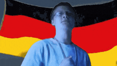 a man wearing glasses stands in front of a large german flag