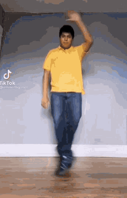 a young man in a yellow shirt and blue jeans is dancing in a room .