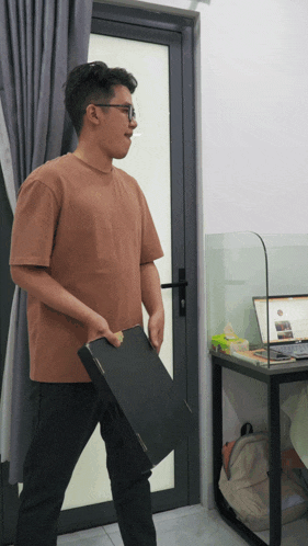 a man in a brown shirt is holding a black box in front of a glass door
