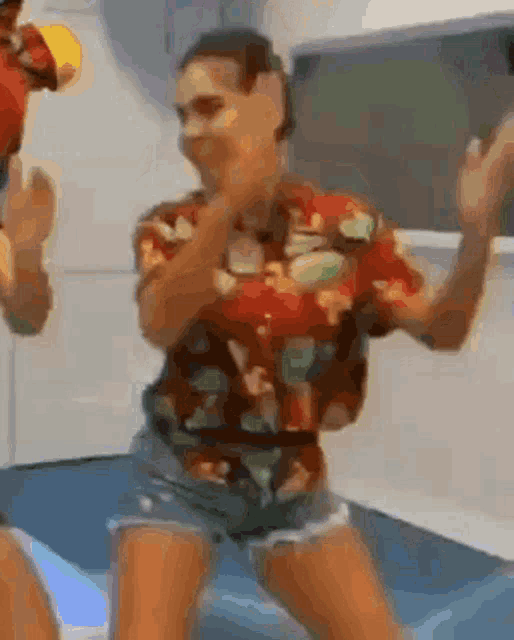 a man in a hawaiian shirt and shorts is dancing with a woman .