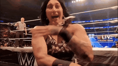 a woman is standing in a wrestling ring with a referee standing behind her .