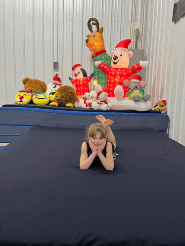 a little girl is laying on a mat in front of stuffed animals