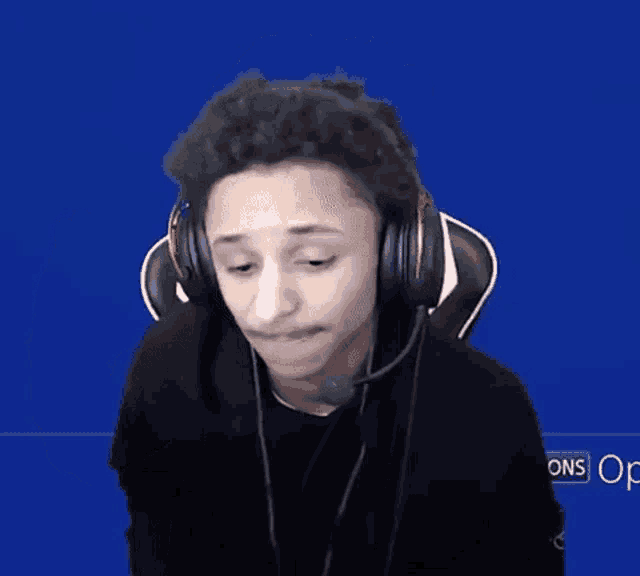 a man wearing headphones and a microphone waves his hand in front of a blue screen