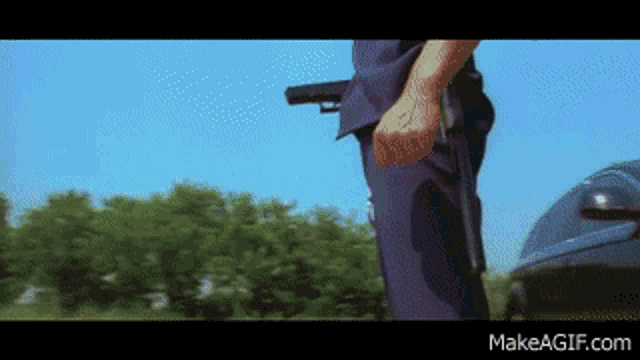 a man holding a gun in front of a car with makeagif.com on the bottom