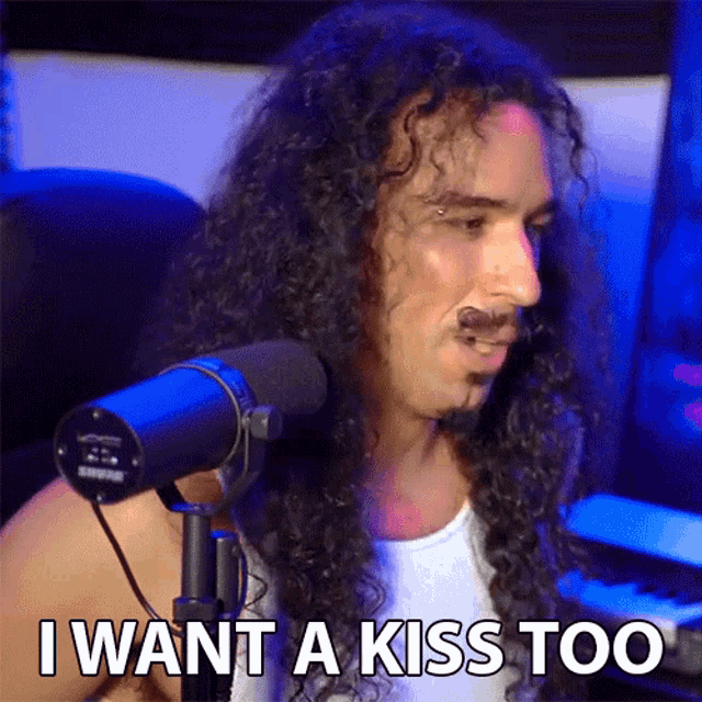 a man with long curly hair is sitting in front of a shure microphone and says i want a kiss too