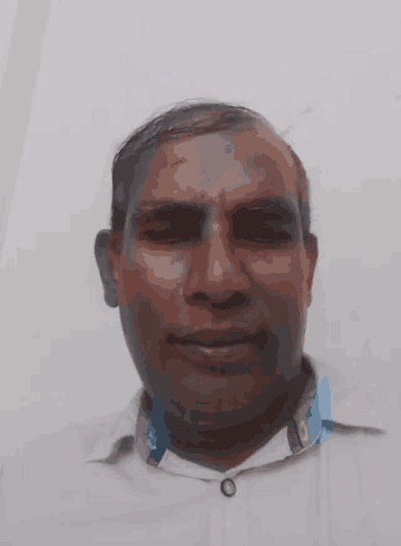 a man in a white shirt with a blue collar looks at the camera with a white background
