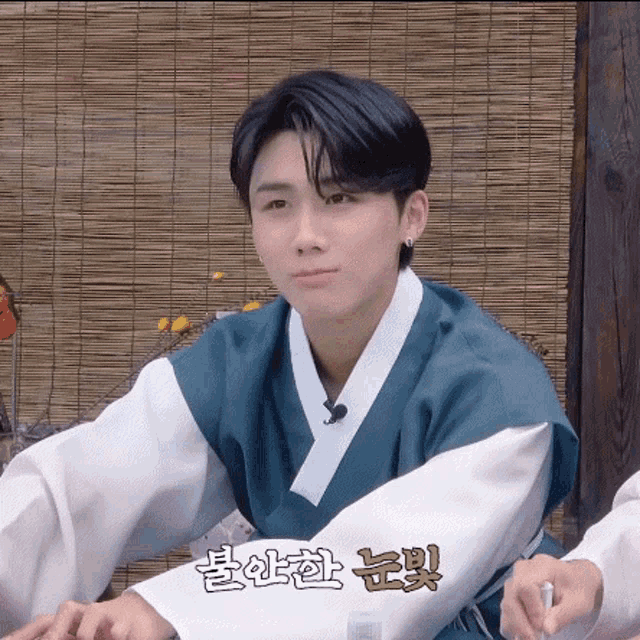 a young man in a traditional korean dress is sitting in front of a bamboo screen .