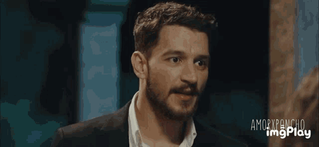 a man with a beard in a suit and white shirt is looking at the camera with the words amorxponcho imgplay below him