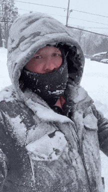 a person wearing a hooded jacket and a scarf is standing in the snow