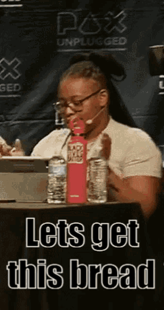 a woman is sitting at a table with a water bottle and a sign that says lets get this bread