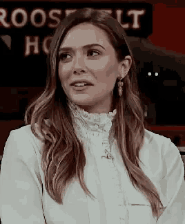 a woman wearing a white shirt and earrings is sitting in front of a red sign .