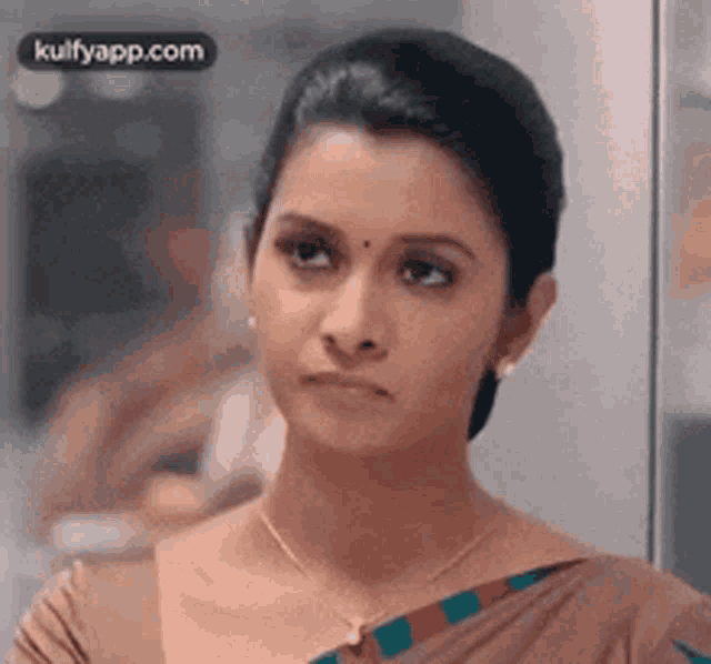 a woman wearing a necklace and earrings is looking at the camera with a sad look on her face .