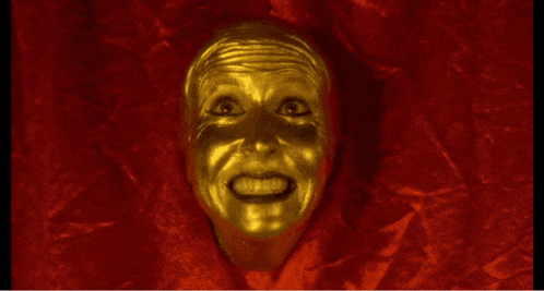 a gold face with a red background is smiling and looking at the camera